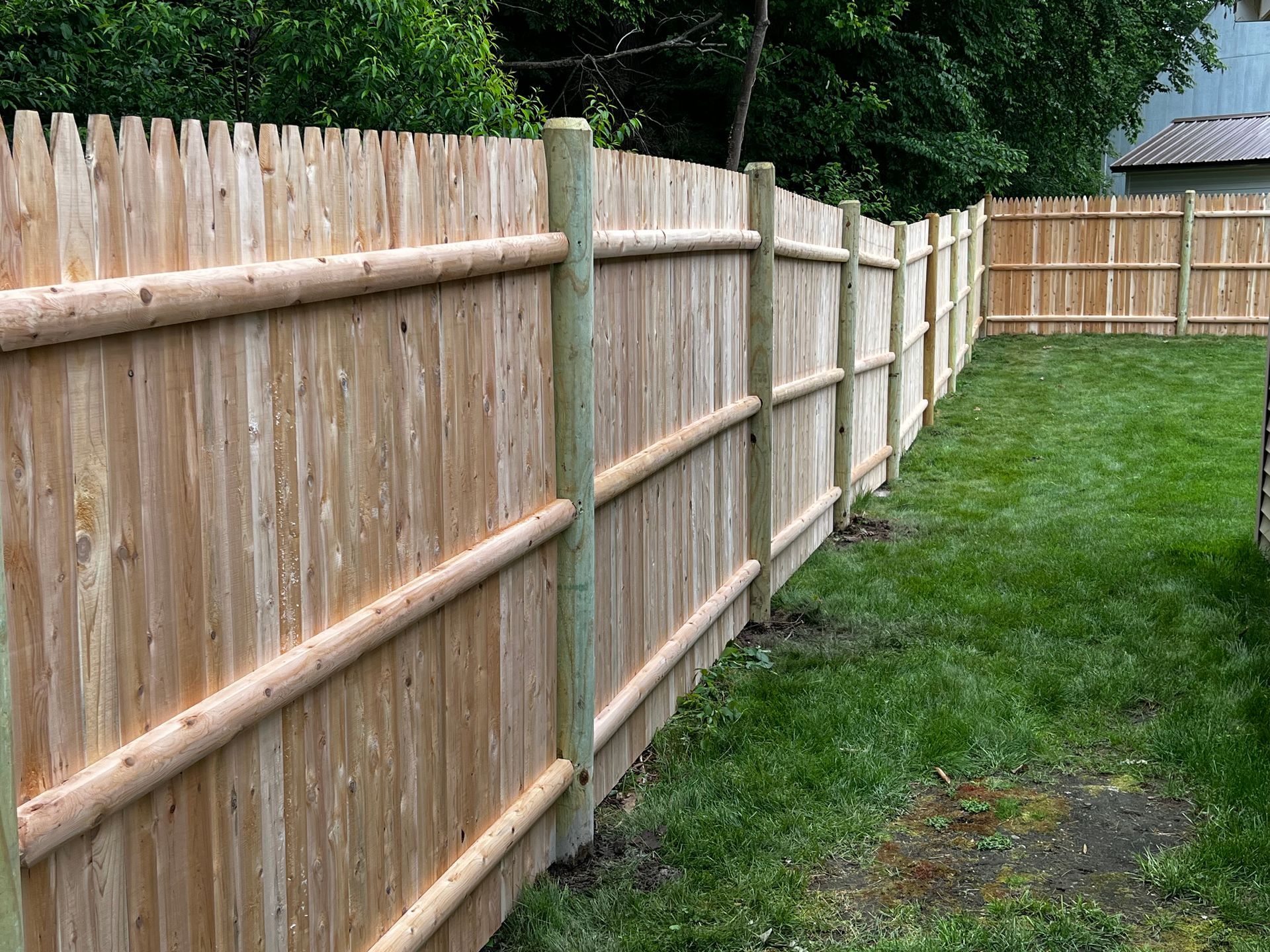 Wooden fence in a grassy yard, with vertical posts and horizontal log-like rails.