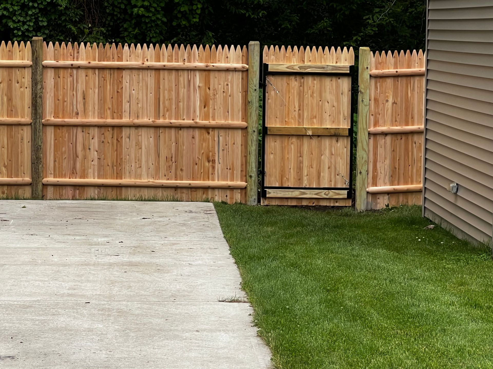 Wooden fence with gate, concrete patio, and green grass.