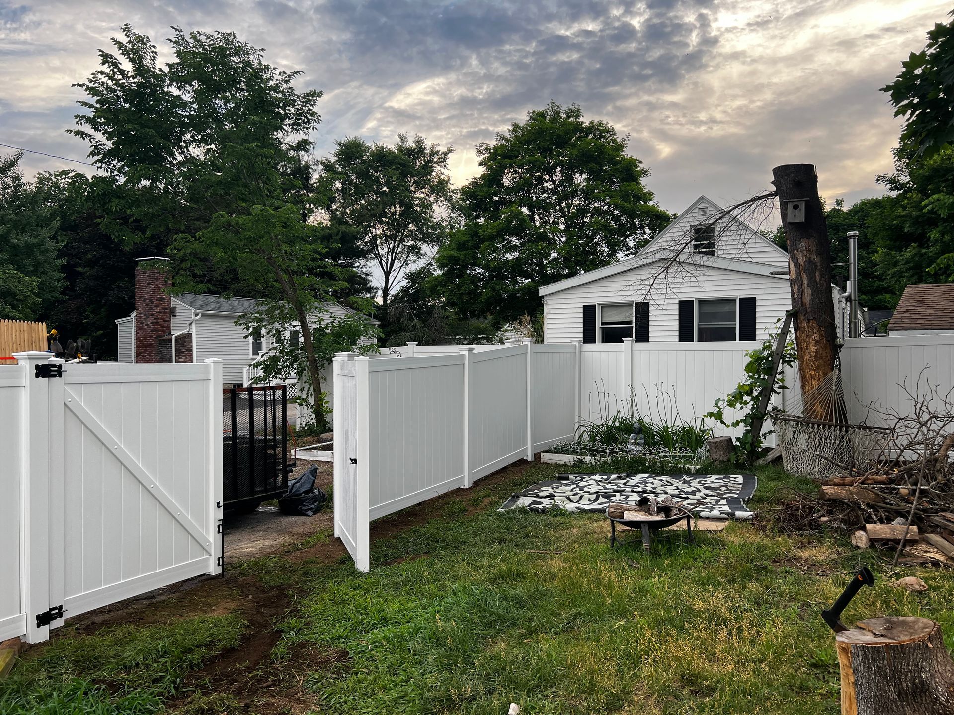 White picket fence enclosing a grassy yard with a small house in the background and a cloudy sky above.
