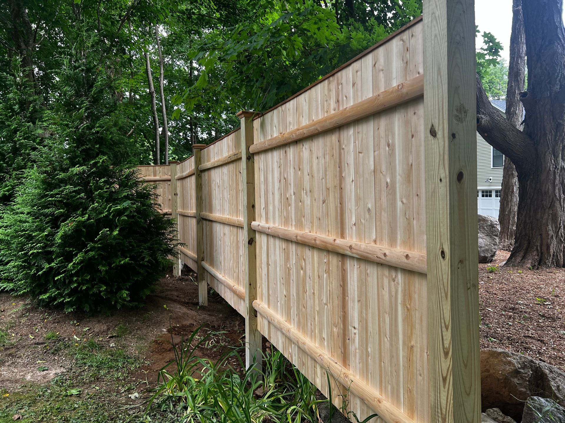 Wooden fence in a yard, next to trees.