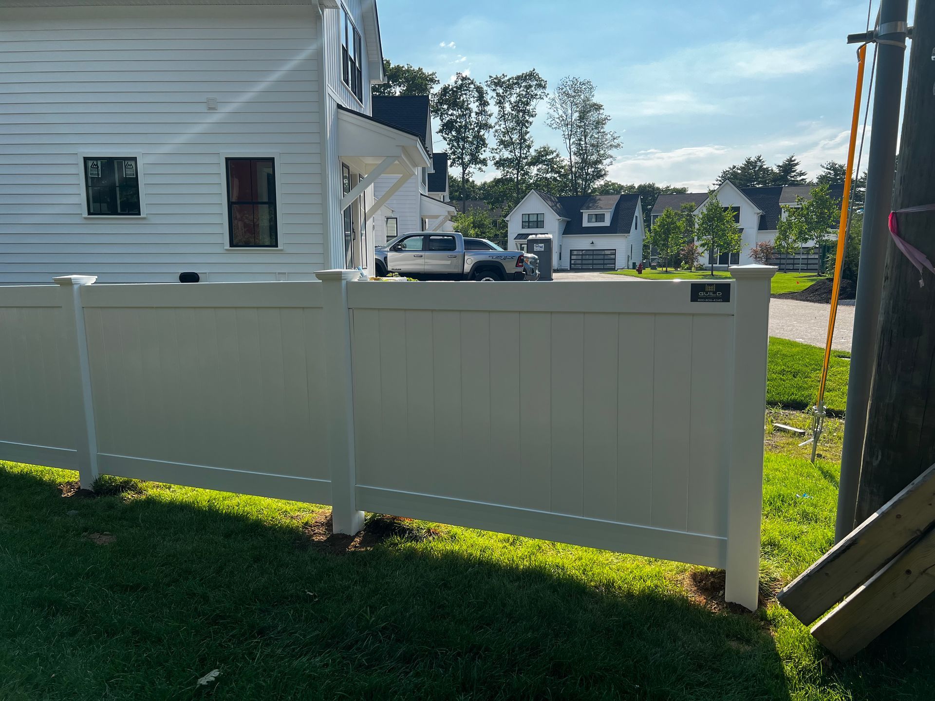 White vinyl fence in front of a house, with a truck visible in the distance.