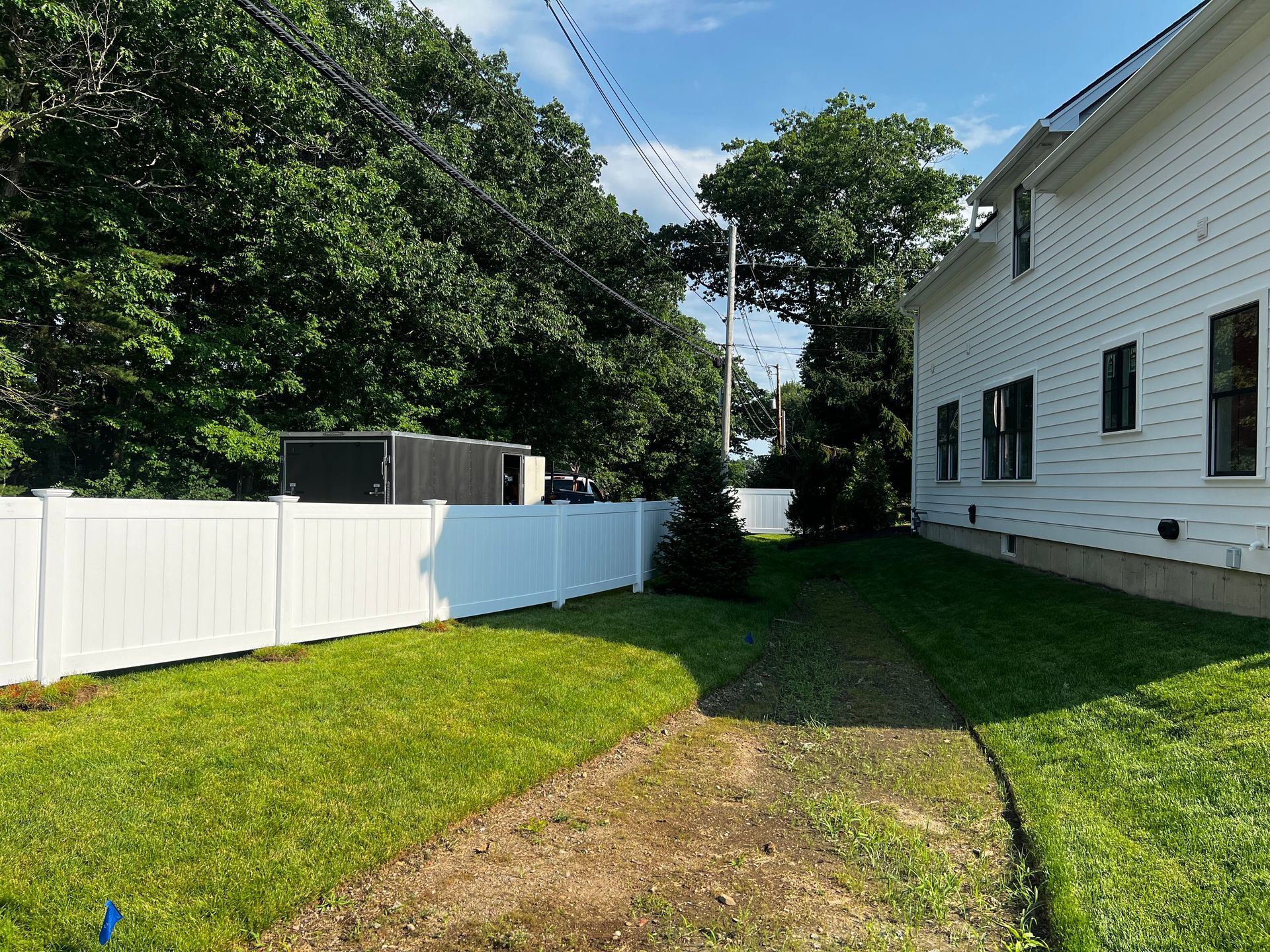 A white fence separates green lawn and a building with black window frames under a blue sky.