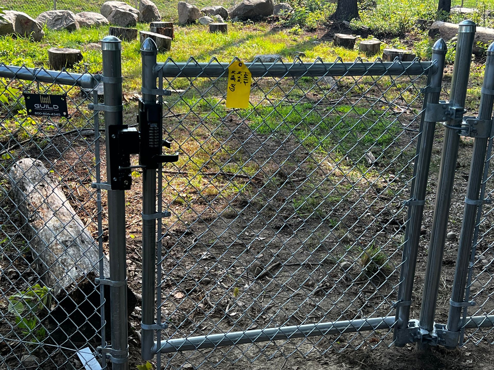 Chain-link gate, closed, with a black latch. Yellow tag hangs from the fence.