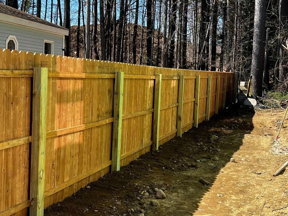 Wooden fence in a wooded area, brown boards with green posts, sunlight.