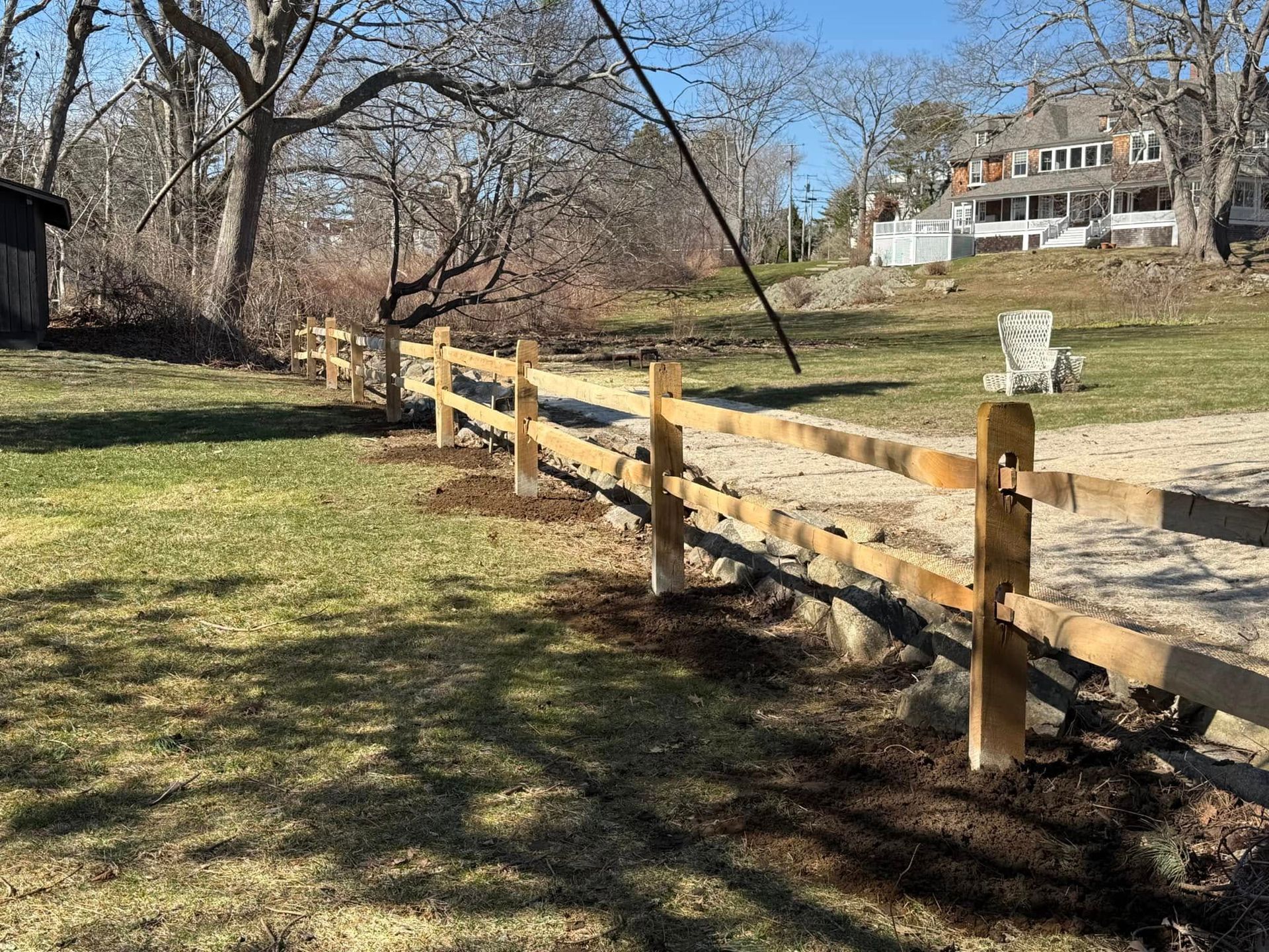 Wooden split-rail fence in a grassy yard, trees in the background, a house in the distance.