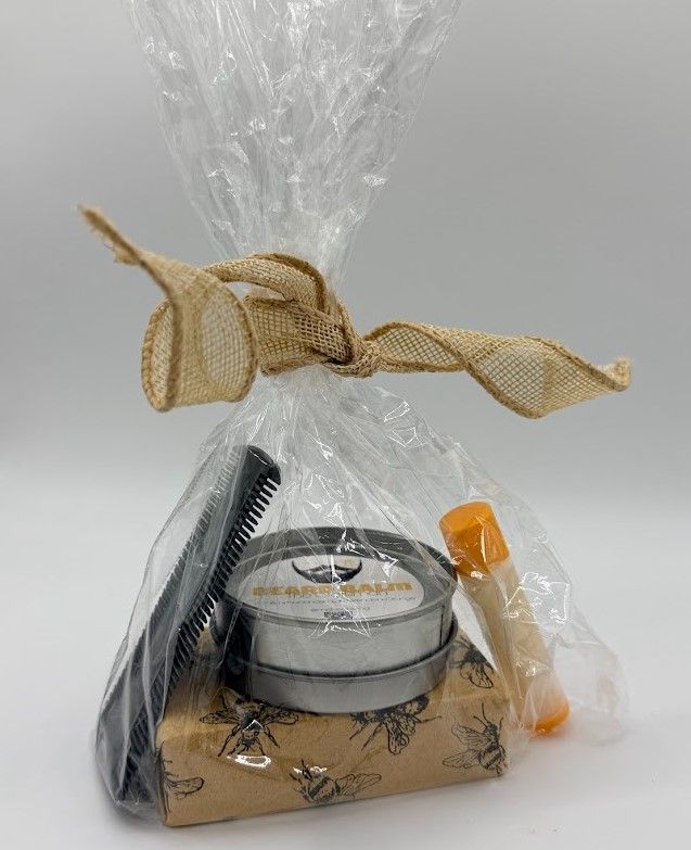 Men’s grooming gift set with beard balm, wooden comb, soap, and lip balm wrapped in clear packaging with burlap bow