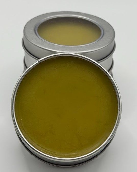 Handcrafted comfrey salve in reusable tin, showing green-gold herbal balm made with homegrown comfrey and beeswax