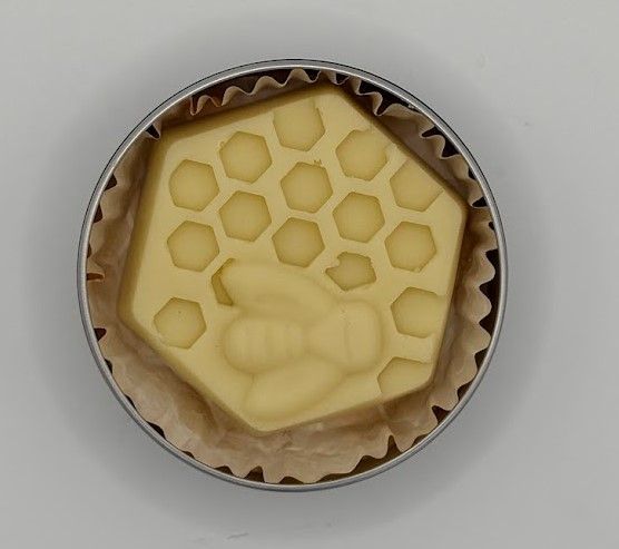 Stack of reusable tins with beeswax honeycomb lotion bars, showing detailed hexagon and bee design on the bar