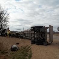 Rolled-over semi-truck on roadside. Firefighters assess the scene on a cloudy day.