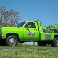 Bright green tow truck on grass with a blue sky background.