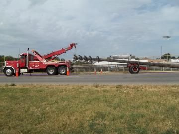 Red tow truck hauling a long, cylindrical object on a flatbed trailer on a road.