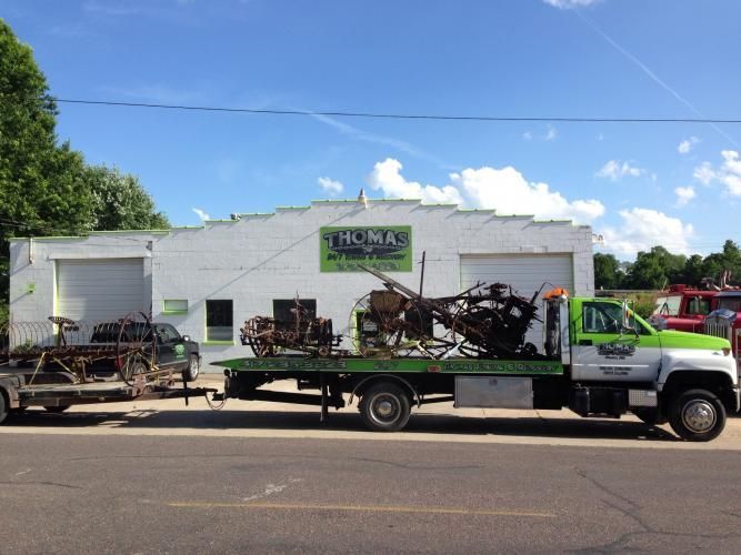 A tow truck parked in front of a white building with green lettering; it carries two loads of metal.