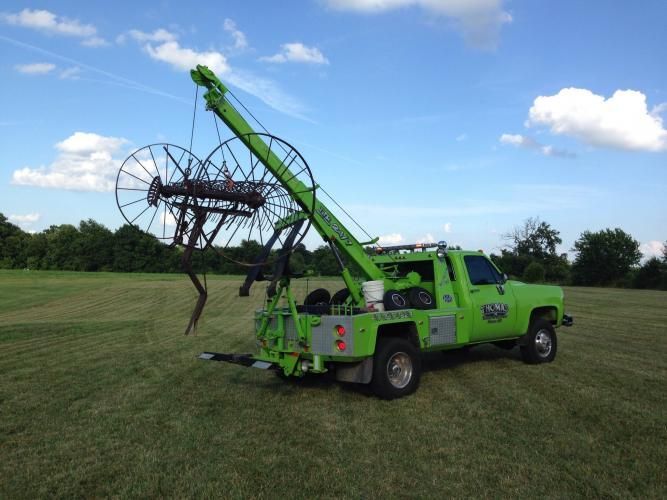 Green tow truck with a unique towing apparatus in a field.