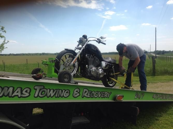 Motorcycle being secured onto a tow truck by a person in a rural setting.