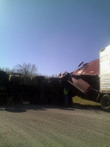 Truck tipped over, cargo spilled on the ground, person in high-vis vest inspects the scene.