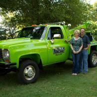 A bright green tow truck with two people posing in front of it in a grassy area.