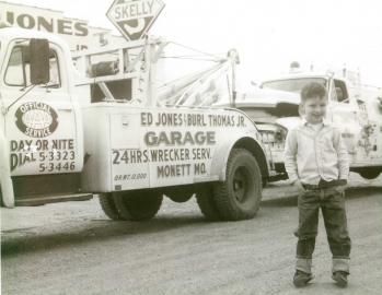Young boy stands beside a vintage tow truck with