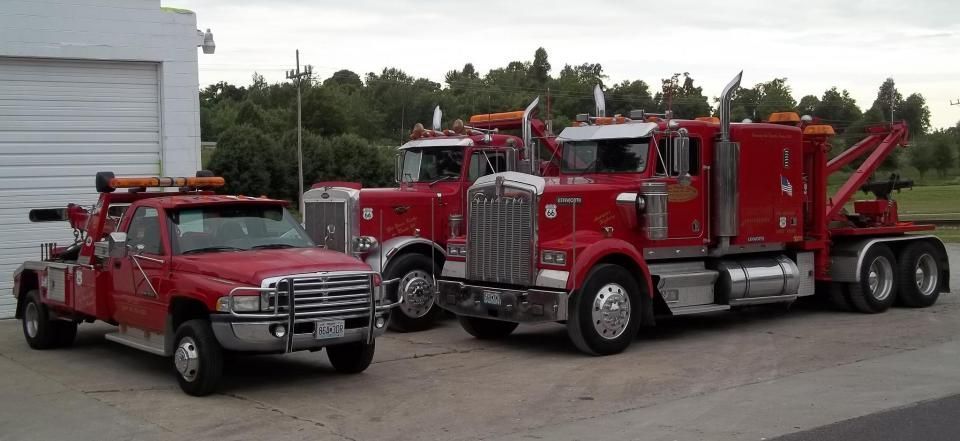 Three red tow trucks parked outdoors. One is a smaller truck, two are semi-truck size. All have lights on top.