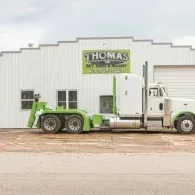 White and green semi-truck in front of Thomas 24/7 service garage, with a white exterior.