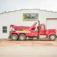 Red tow truck in front of a building with the business name