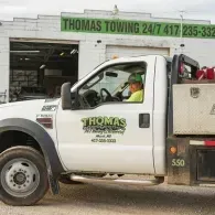 White Thomas Towing truck with driver; building with business sign in background.