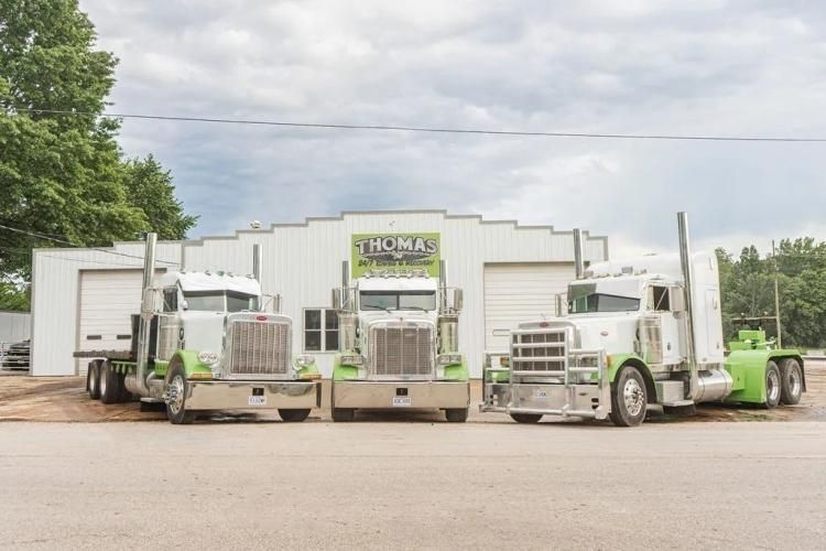 Three green and white semi-trucks parked in front of a white building with a company logo.