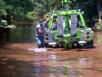 A tow truck is partially submerged in water, and a man wades in front of it.