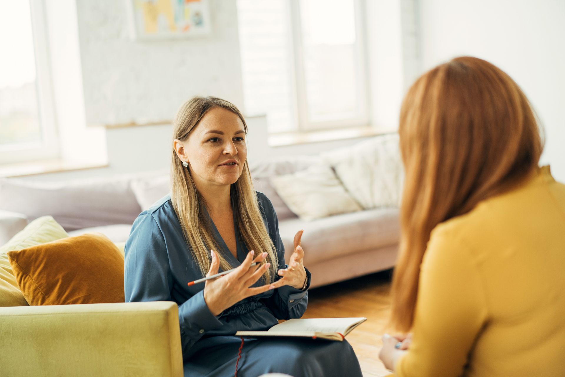 A female psychologist listens attentively to a woman during a therapy session in a calm office.