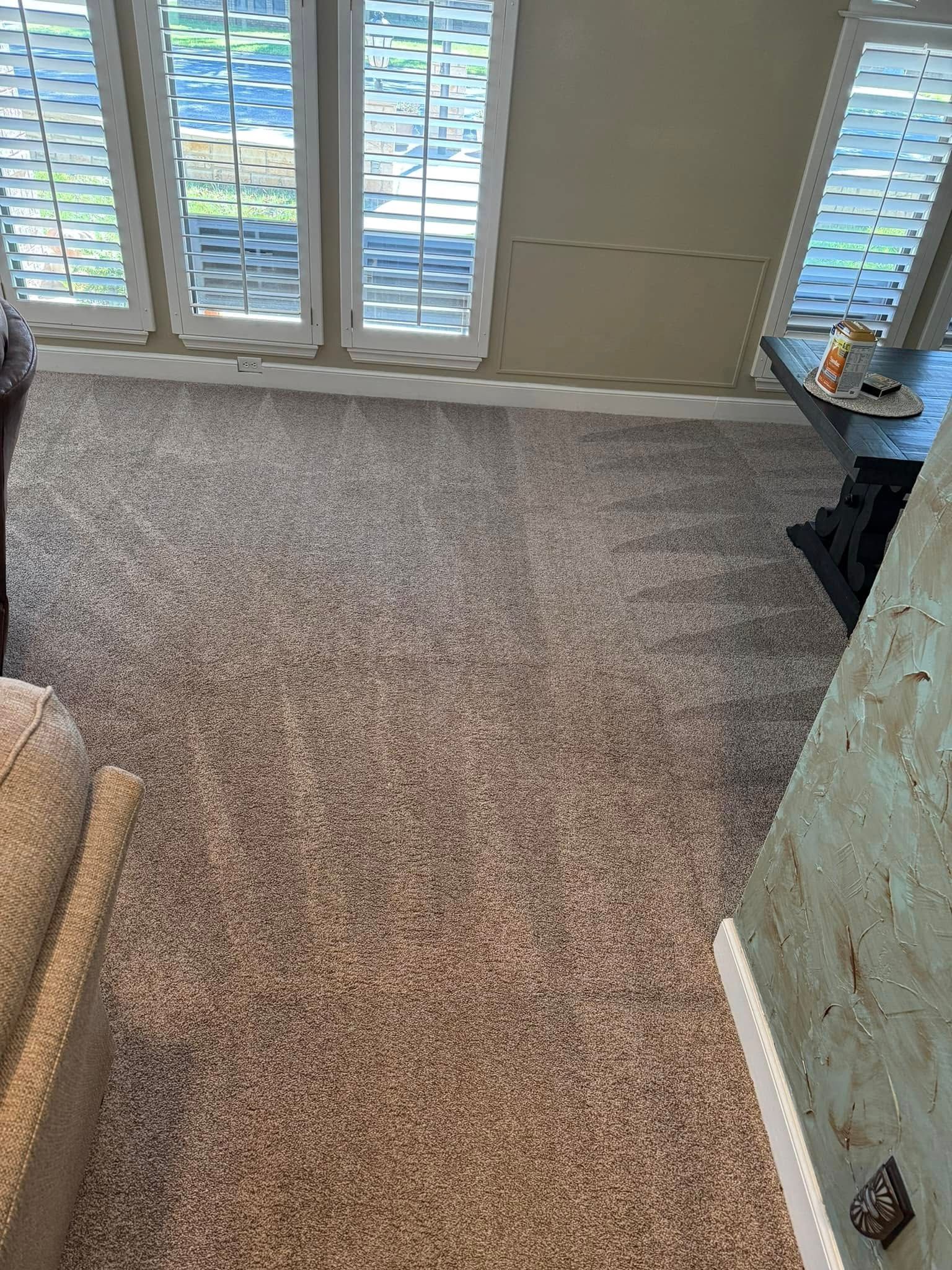 A living room with a carpeted floor and shutters on the windows.