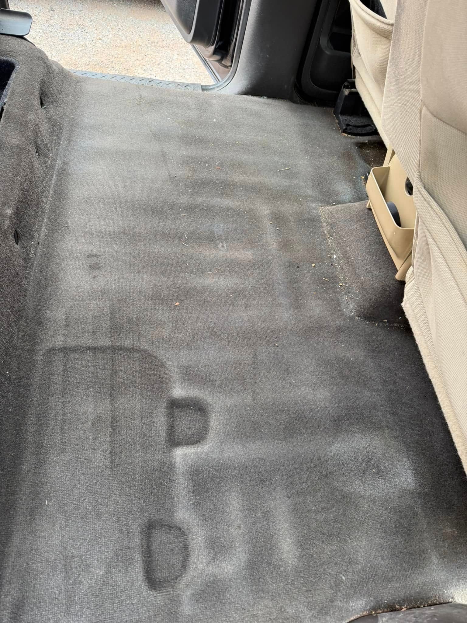 A gray carpeted floor in a car with a footprint on it.