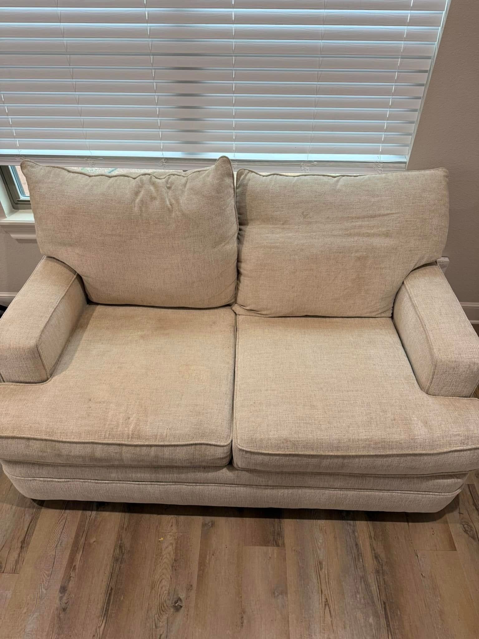 A beige couch is sitting in front of a window in a living room.