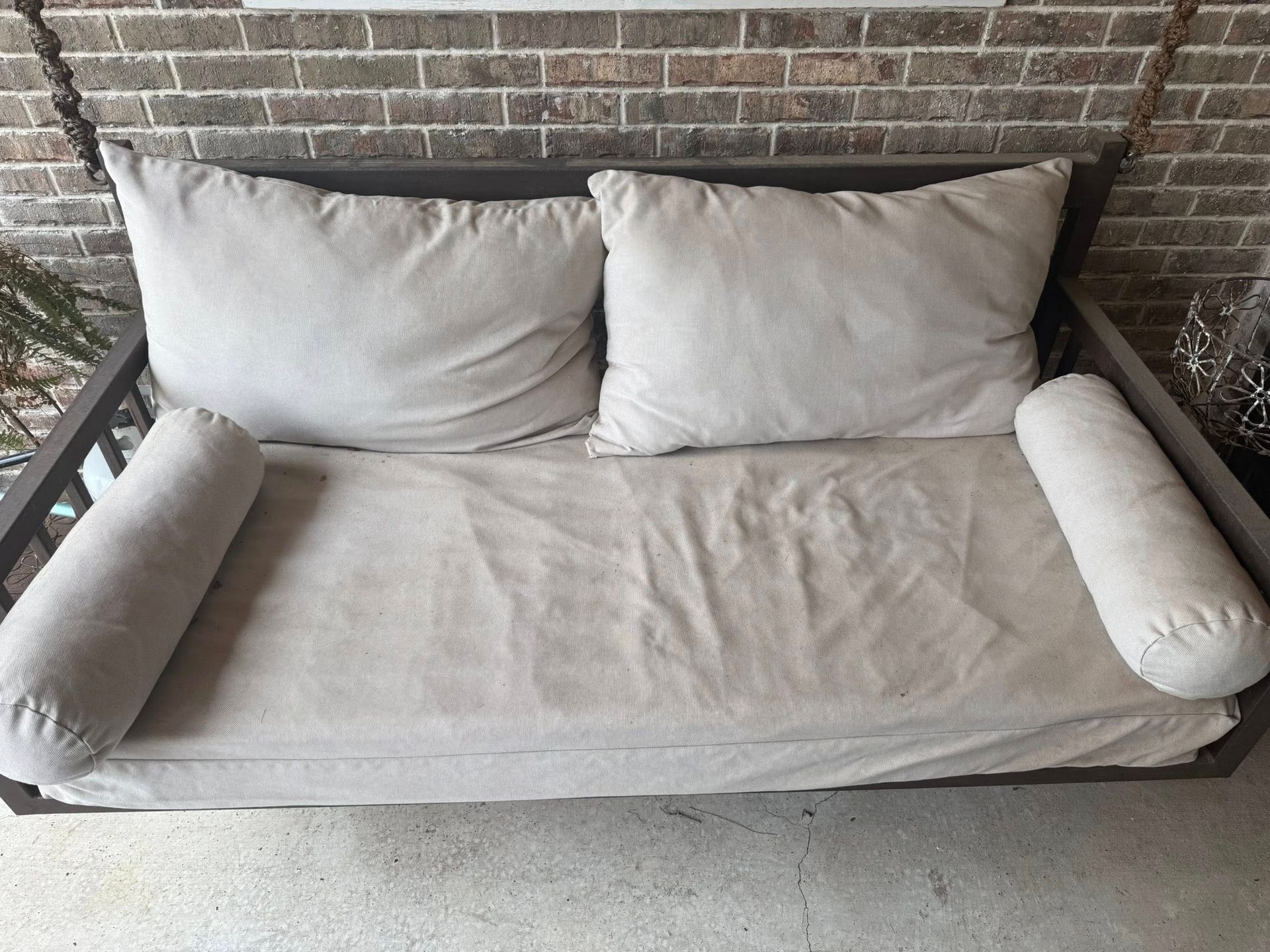 A porch swing with white pillows and a brick wall in the background.