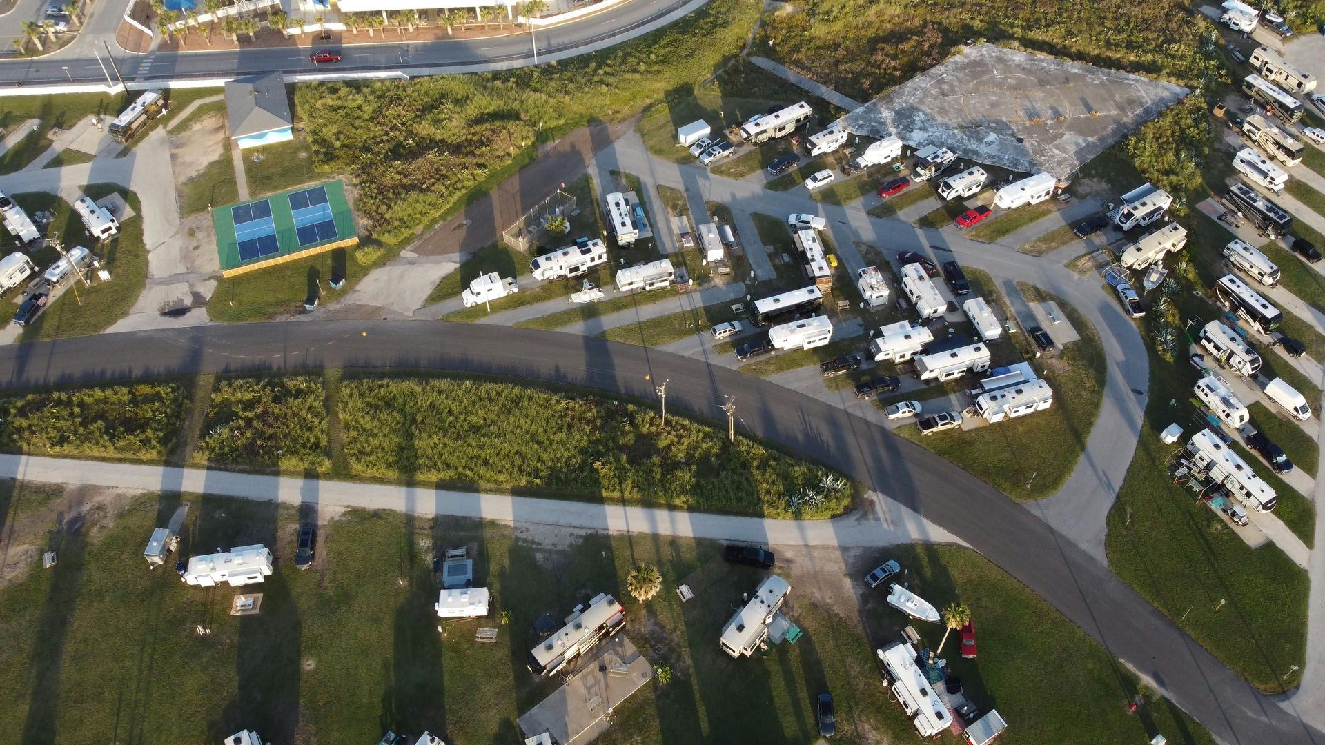 Aerial view of a parking lot with many cars, curved roads, and nearby houses and trees.