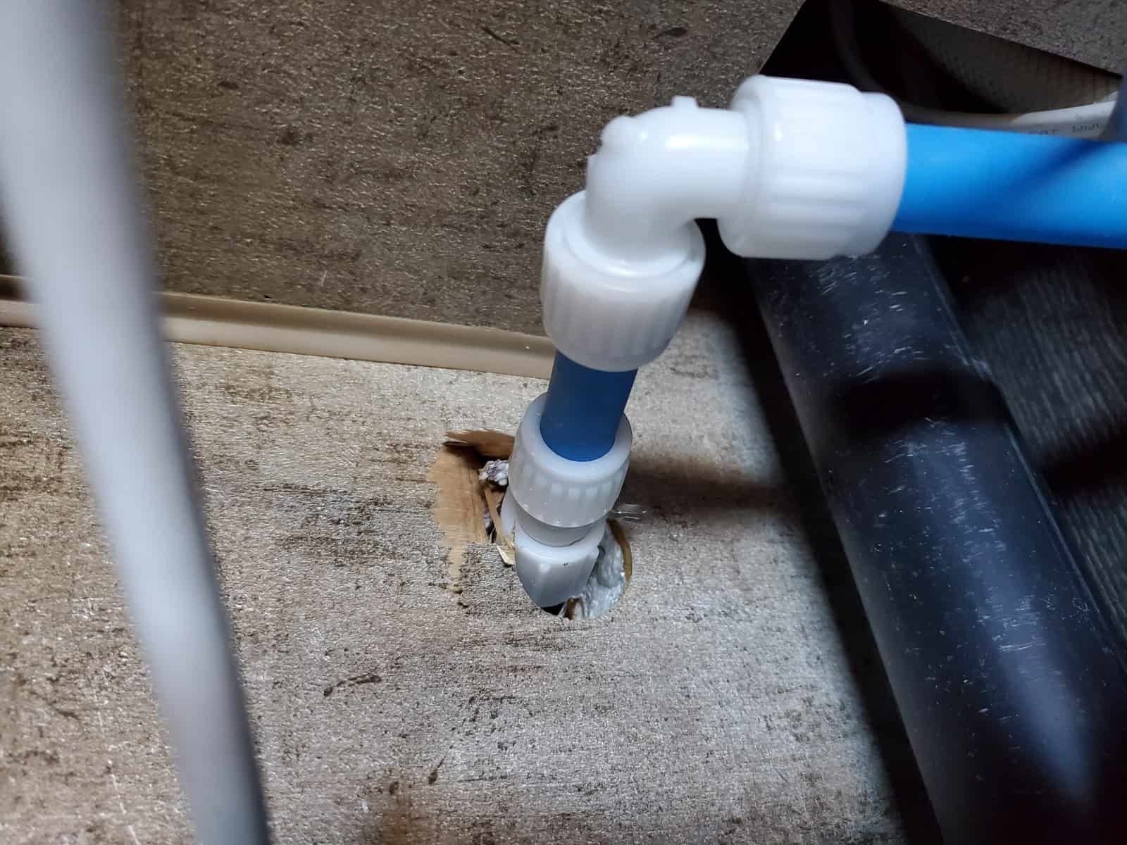 A blue pipe is connected to a white pipe in a hole in the floor.