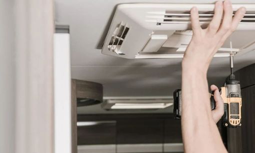 A person is fixing a ceiling fan with a drill.