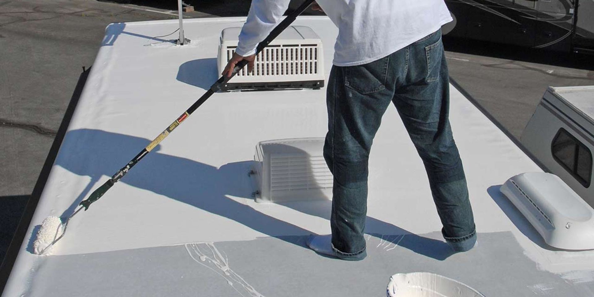A man is painting the roof of a trailer with a brush.