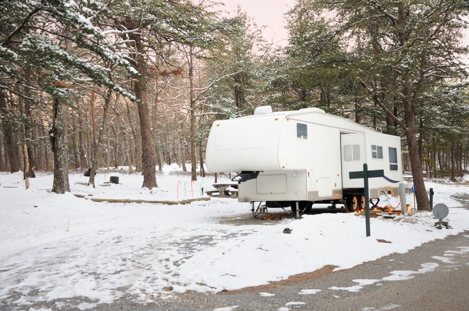 A white rv is parked in the snow in the woods.