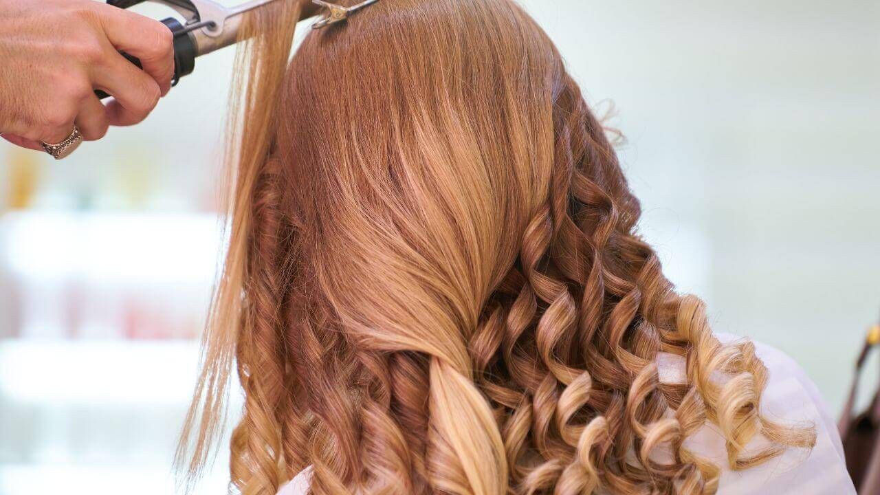 A woman cutting long blonde hair with scissors.