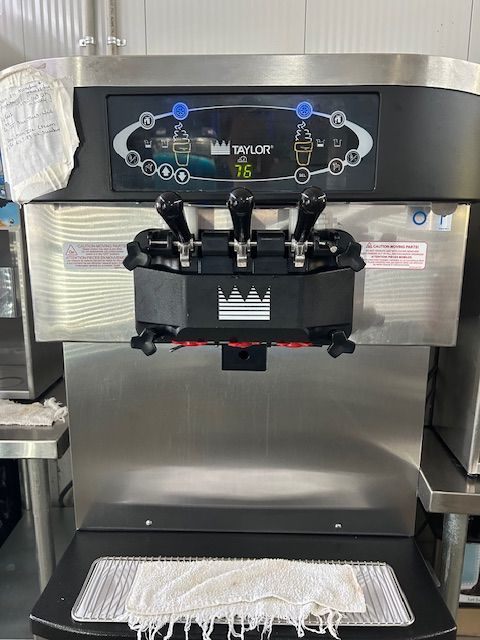 A stainless steel Taylor soft-serve ice cream machine with three dispensing handles and a digital temperature display.