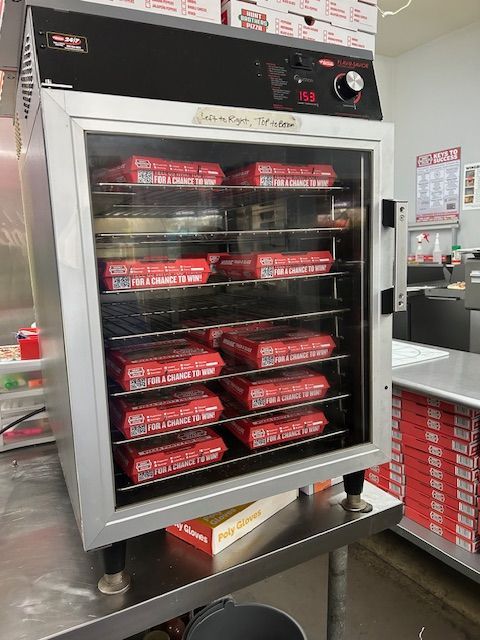 A silver commercial food warmer containing stacked boxes of pizza sits on a metal table in a kitchen.
