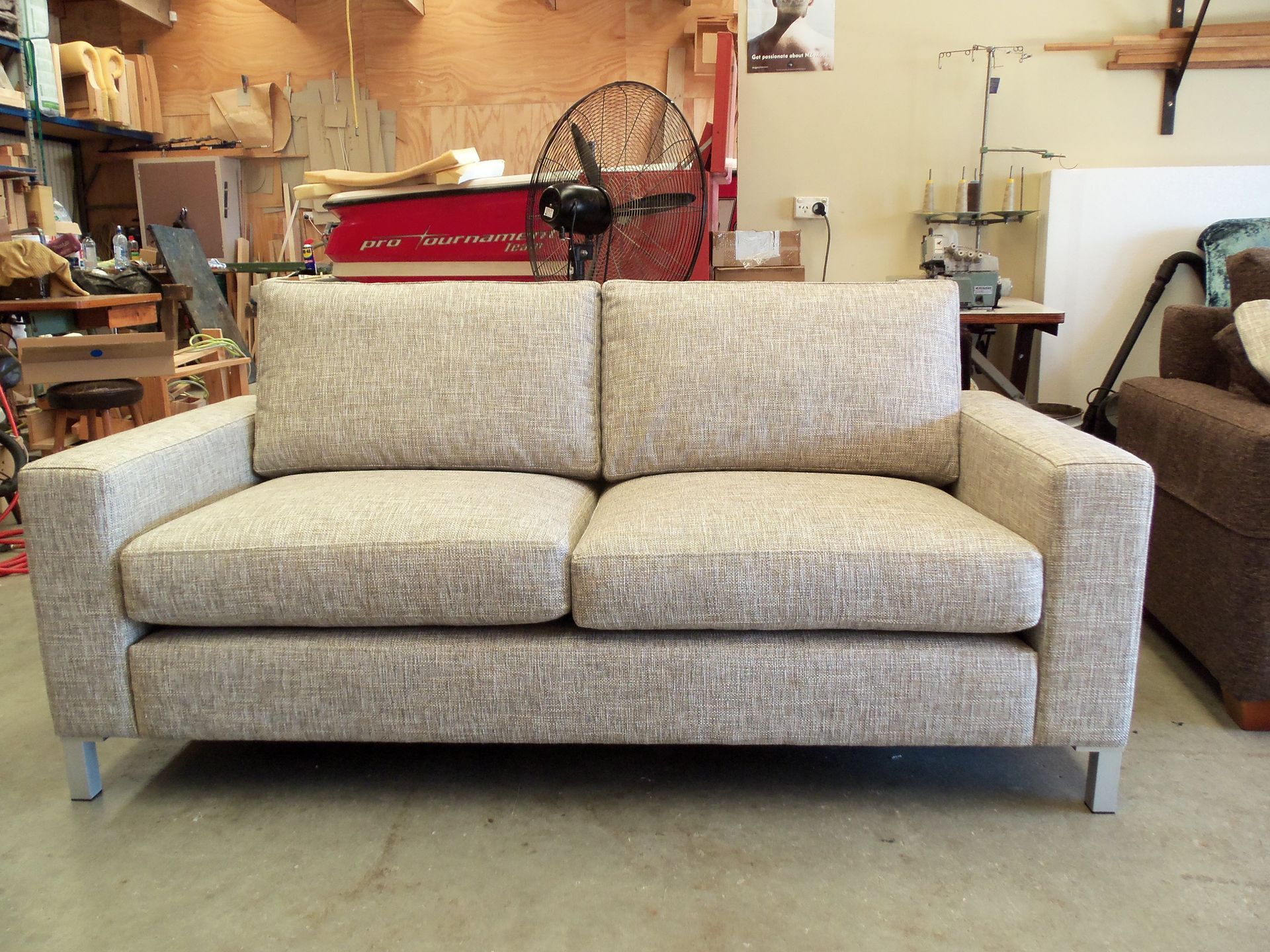 A couch is sitting in a room with a fan in the background