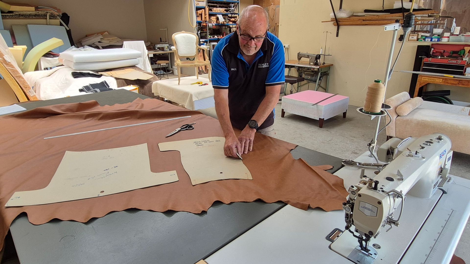 A man is cutting a piece of leather in front of a sewing machine