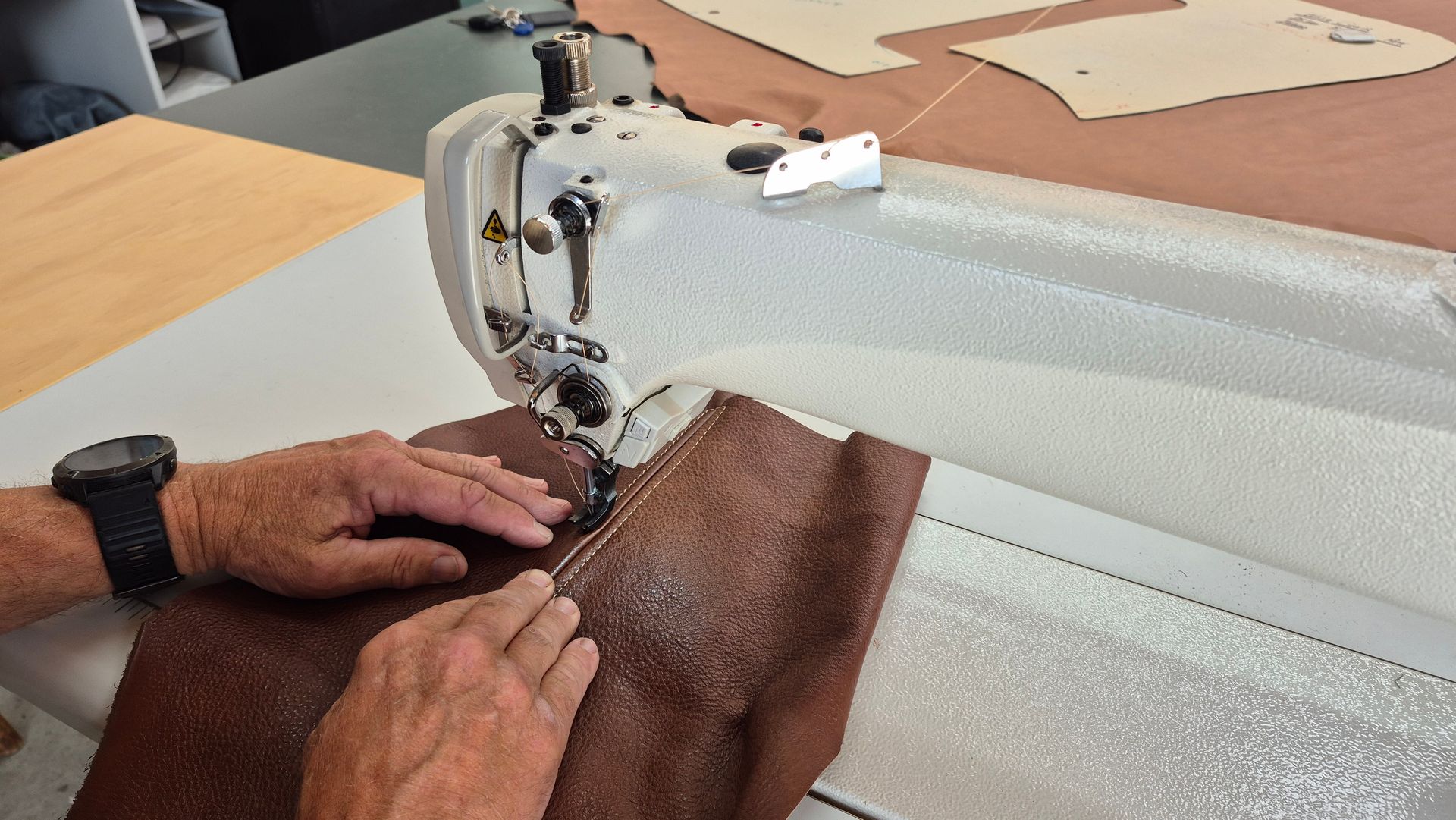 A man is using a sewing machine to sew a piece of brown fabric.