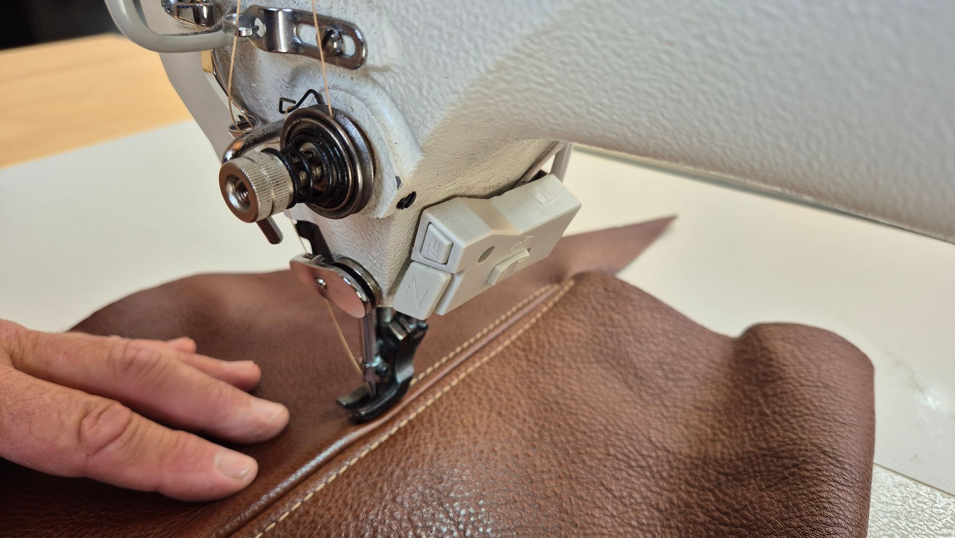 A person is using a sewing machine to sew a piece of brown leather.