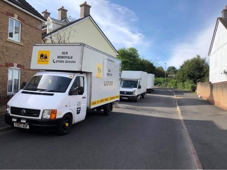 Two white moving vans parked on a residential street. One has yellow branding. Sunny day.