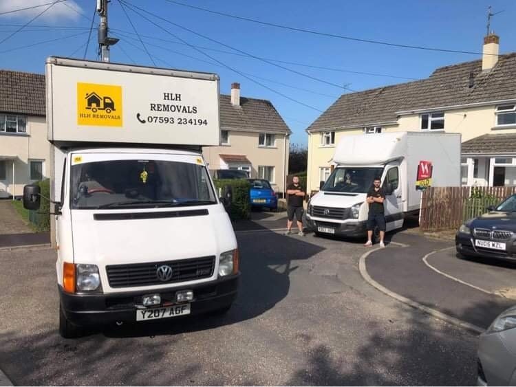 Two white moving vans with workers in a residential setting, under a blue sky.