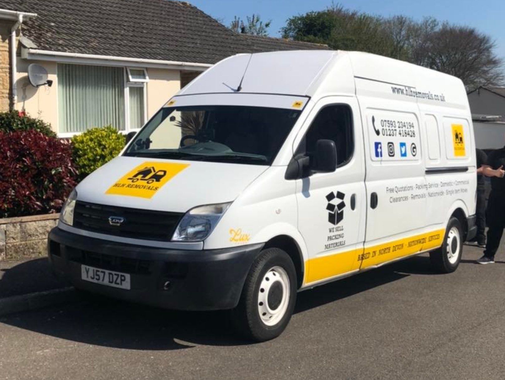 White delivery van parked in front of a house. Has logo with yellow accents and website.