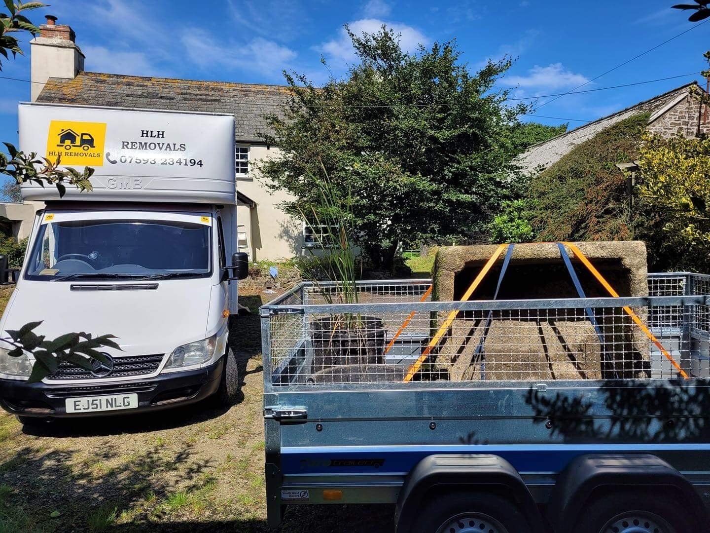 Moving van parked near a house, trailer loaded with hay bale strapped down on sunny day.