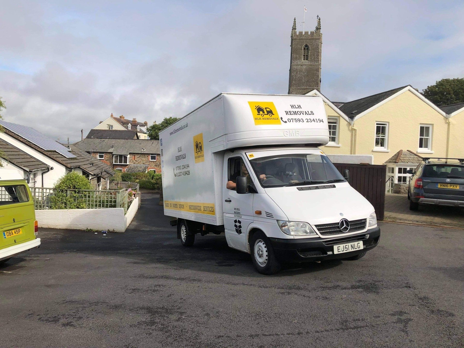 White delivery van on a street, with a church tower in the background.