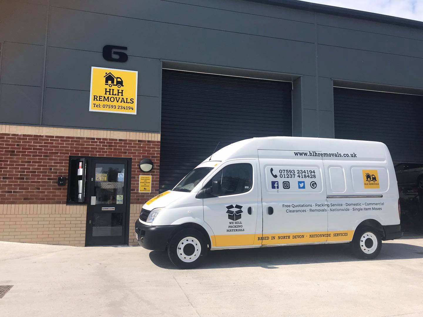 White and yellow removal van parked outside a building with a door and sign.